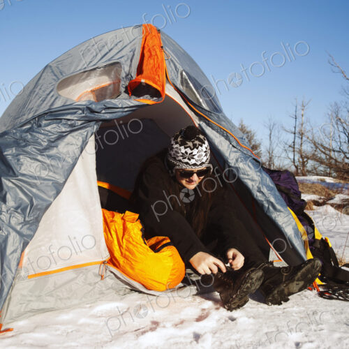 Woman sitting in tent in snowy landscape lacing up snow boots. Woman sitting in tent in snowy landscape lacing up snow boots.