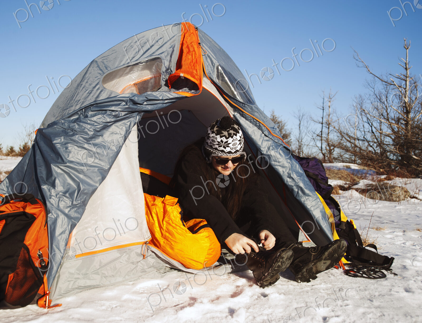 Woman sitting in tent in snowy landscape lacing up snow boots.