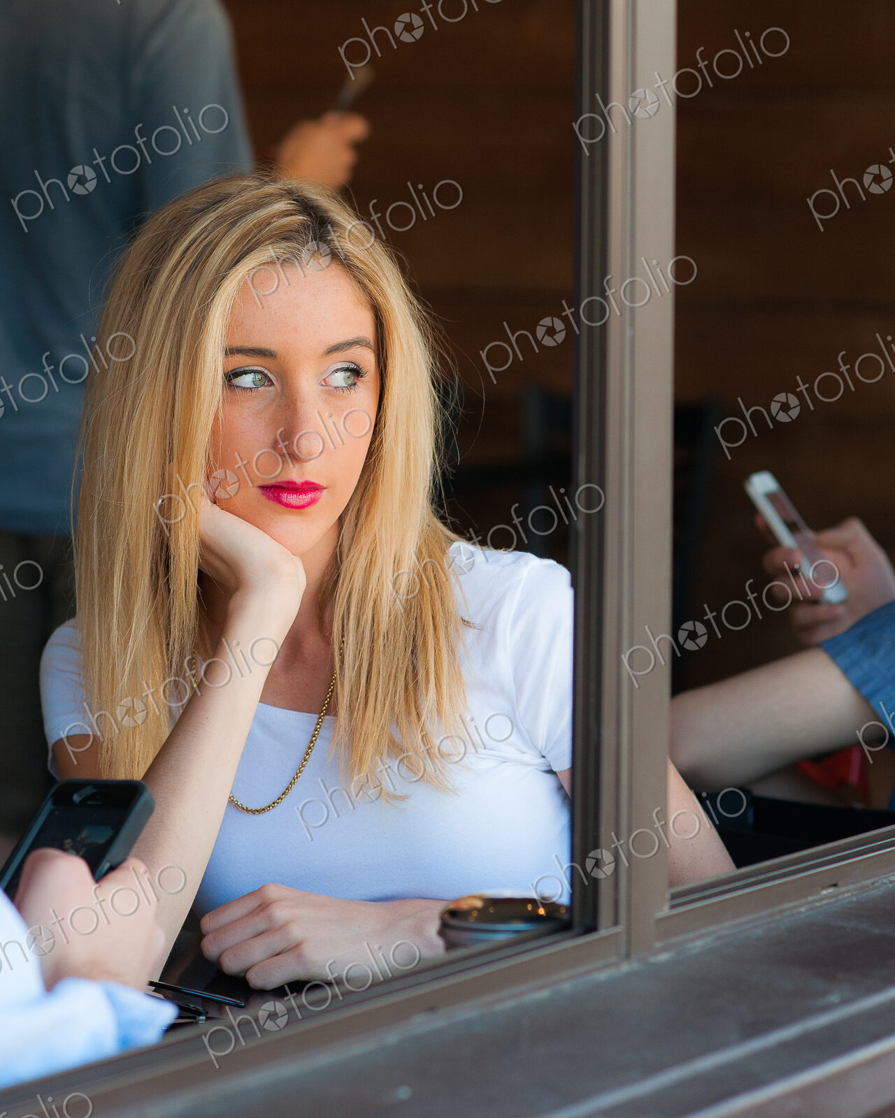 Woman sitting looking out of cafe window while other people use smartphones.