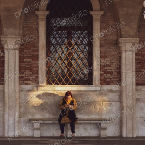 Woman sitting on a bench underneath arched window in Venice, Veneto, Italy.