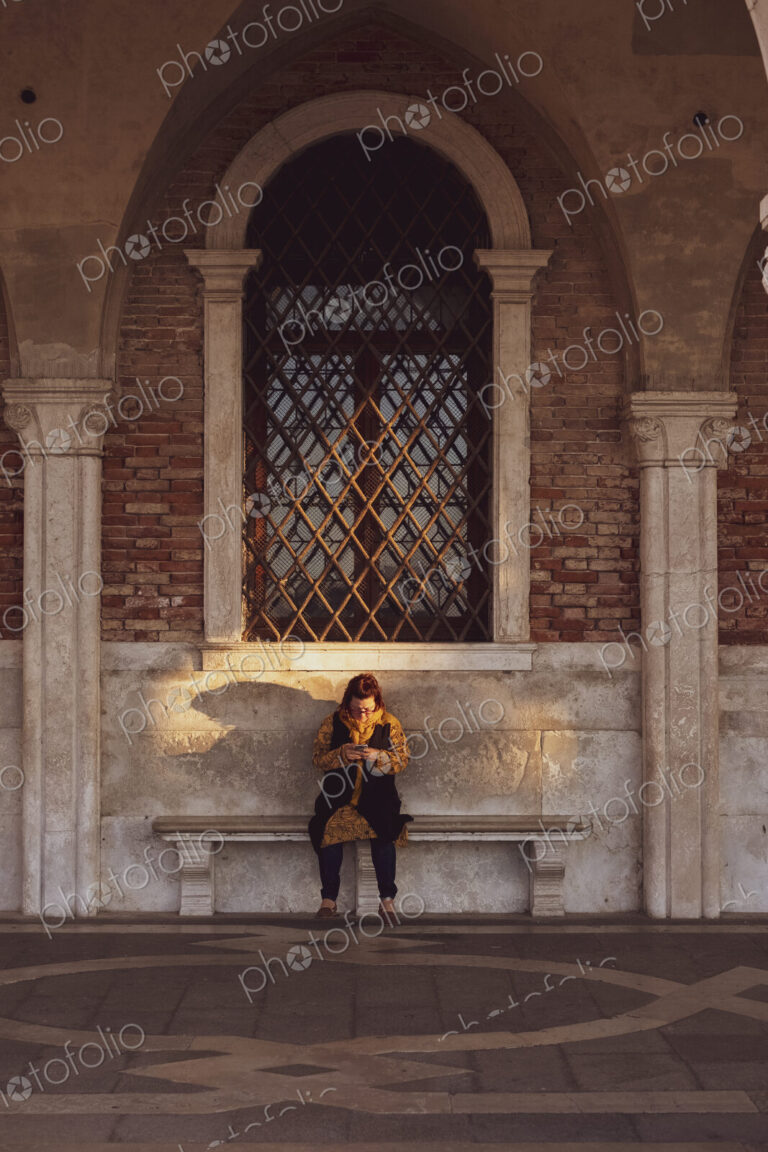 Woman sitting on a bench underneath arched window in Venice, Veneto, Italy.