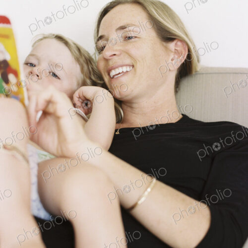 Woman sitting on a sofa, holding a book, reading to her daughter.