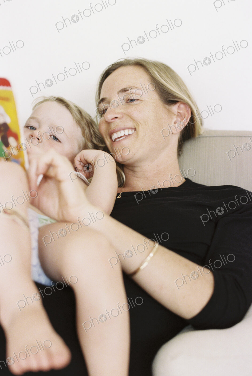 Woman sitting on a sofa, holding a book, reading to her daughter.