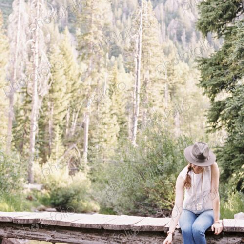 Woman sitting on a wooden bridge over a stream.