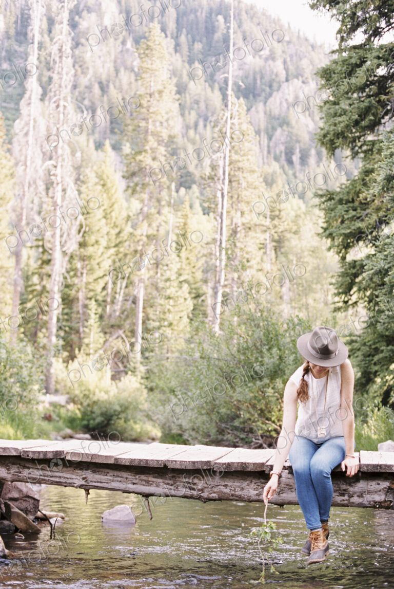 Woman sitting on a wooden bridge over a stream.