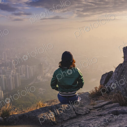 Woman sitting on rock in hills above Hong Kong looking down over the city.