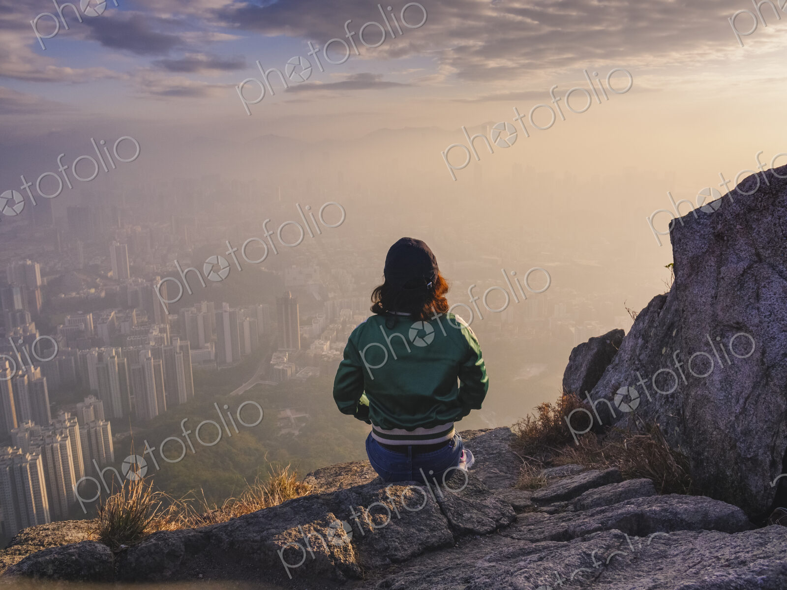 Woman sitting on rock in hills above Hong Kong looking down over the city.