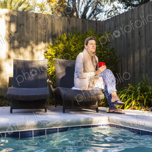 Woman sitting on sun lounger by a swimming pool