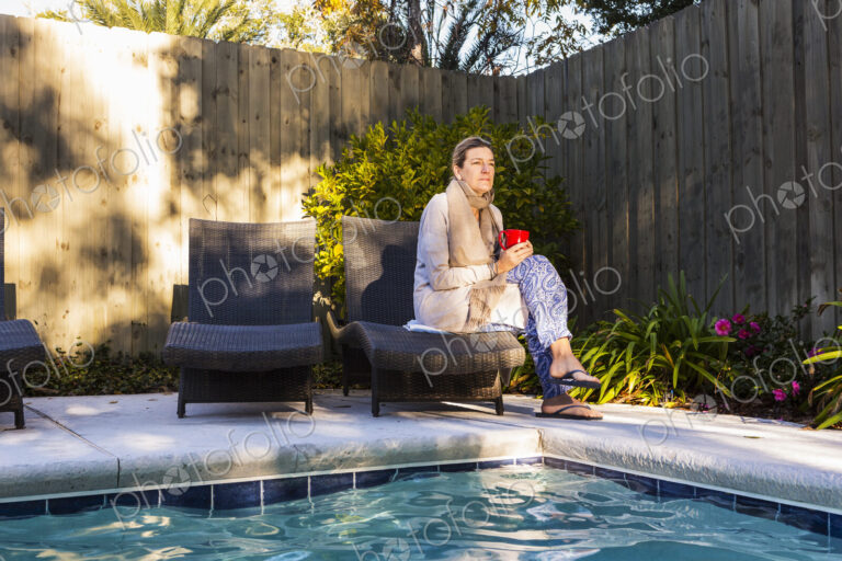 Woman sitting on sun lounger by a swimming pool