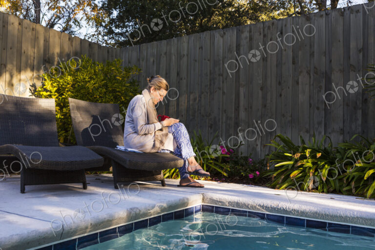 Woman sitting on sun lounger by a swimming pool