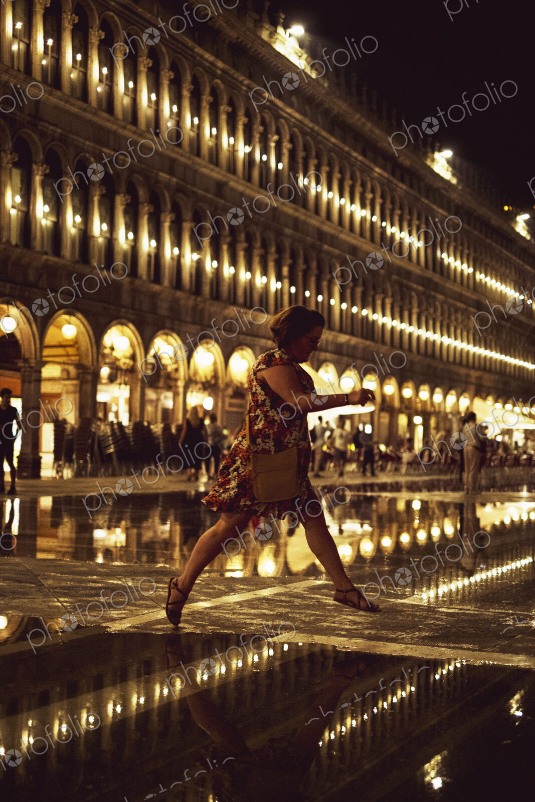 Woman skipping across an illuminated St Marks Square in Venice, Veneto, Italy, at night.
