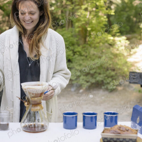 Woman standing at a table in a garden, making coffee.