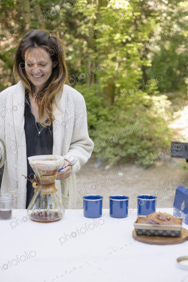 Woman standing at a table in a garden, making coffee.