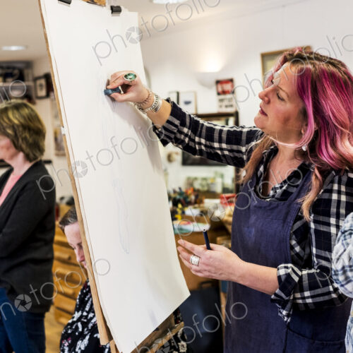 Woman standing at an easel, drawing a human leg at a life drawing glass.