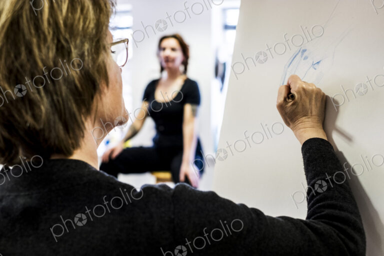 Woman standing at easel, drawing human hand at life drawing class