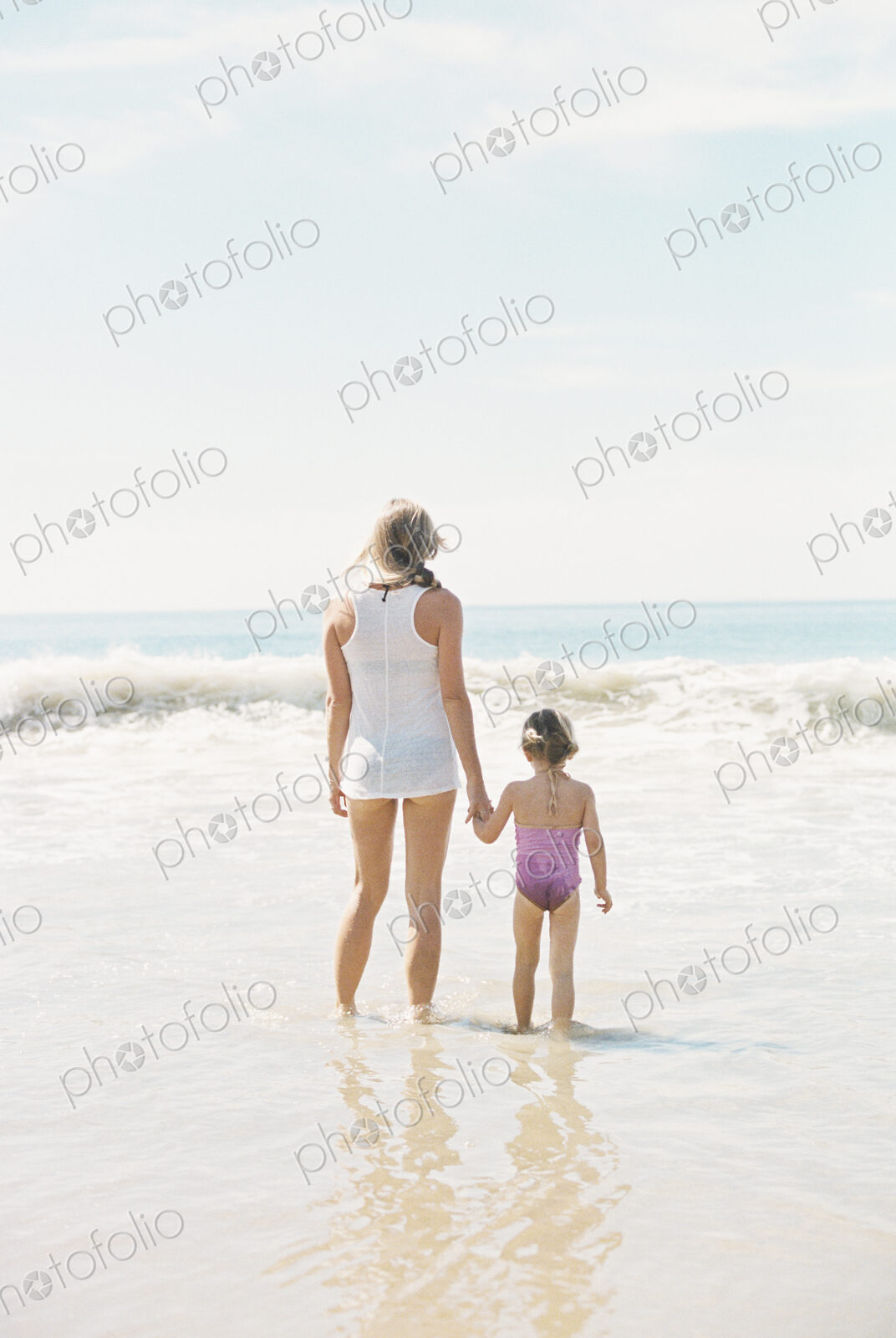 Woman standing hand in hand with her daughter on a sandy beach.