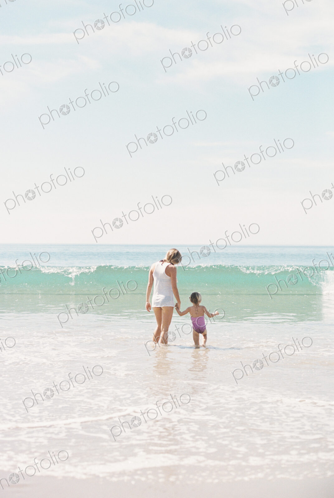 Woman standing hand in hand with her daughter on a sandy beach watching a wave.