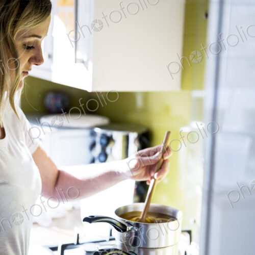 Woman standing in a domestic kitchen, making jar candles.
