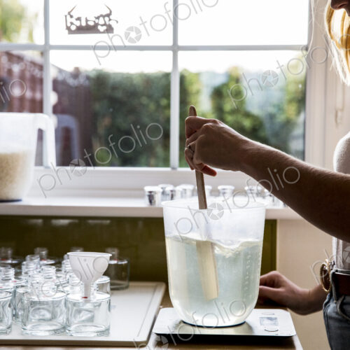 Woman standing in a domestic kitchen, making jar candles.