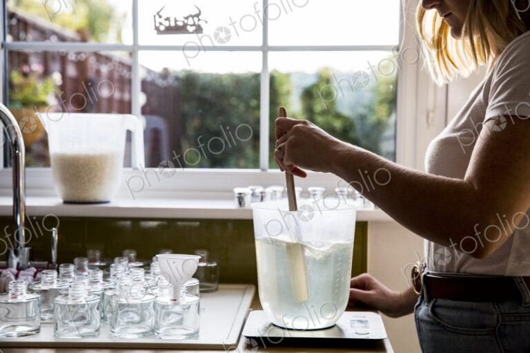 Woman standing in a domestic kitchen, making jar candles.
