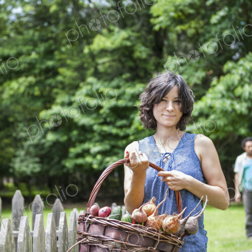 Woman standing in a garden holding a basket of vegetables.