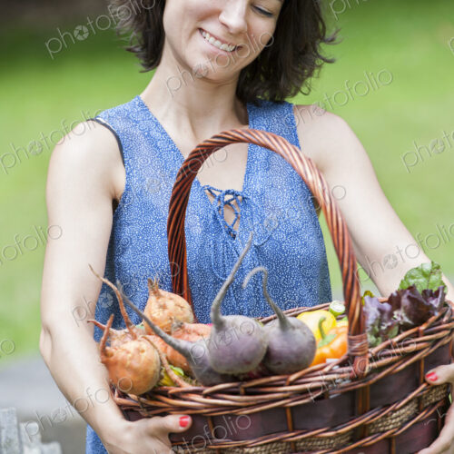 Woman standing in a garden holding a basket of vegetables. Woman standing in a garden holding a basket of vegetables.