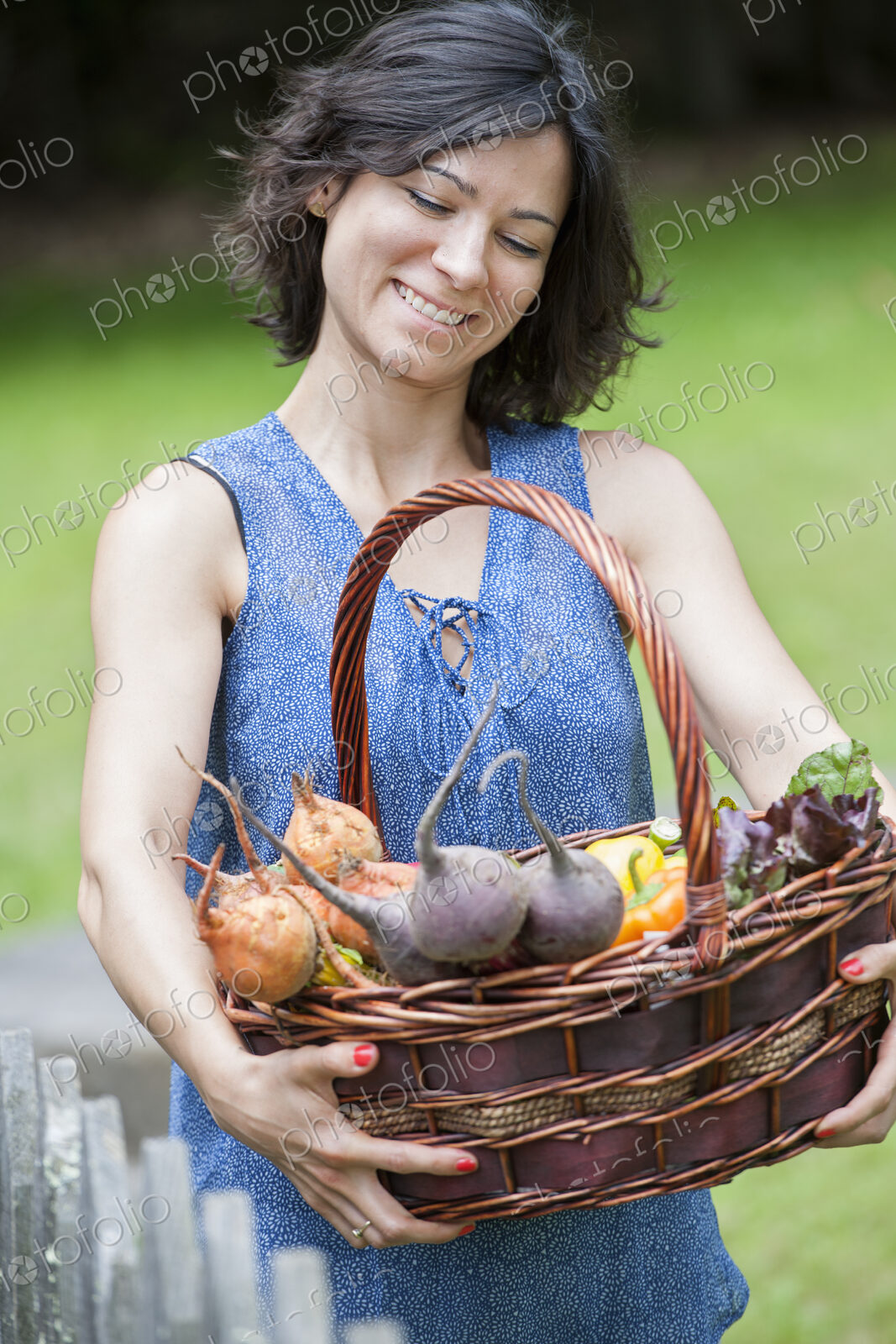 Woman standing in a garden holding a basket of vegetables.