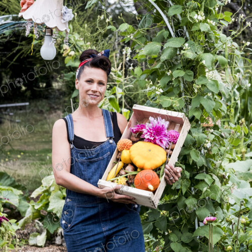 Woman standing in a garden, holding wooden crate with fresh vegetables and flower,… Woman standing in a garden, holding wooden crate with fresh vegetables and flower,…