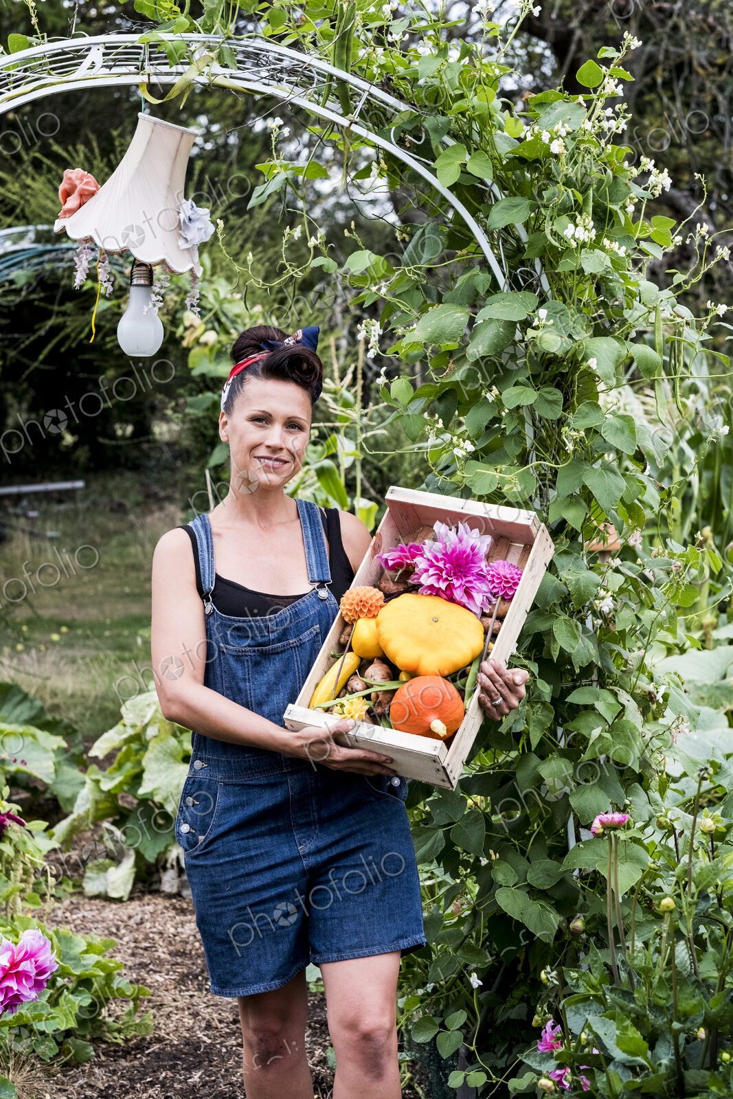 Woman standing in a garden, holding wooden crate with fresh vegetables and flower,…