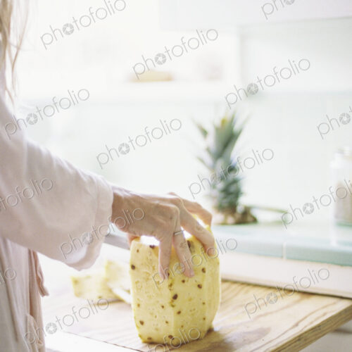 Woman standing in a kitchen, cutting a fresh pineapple.