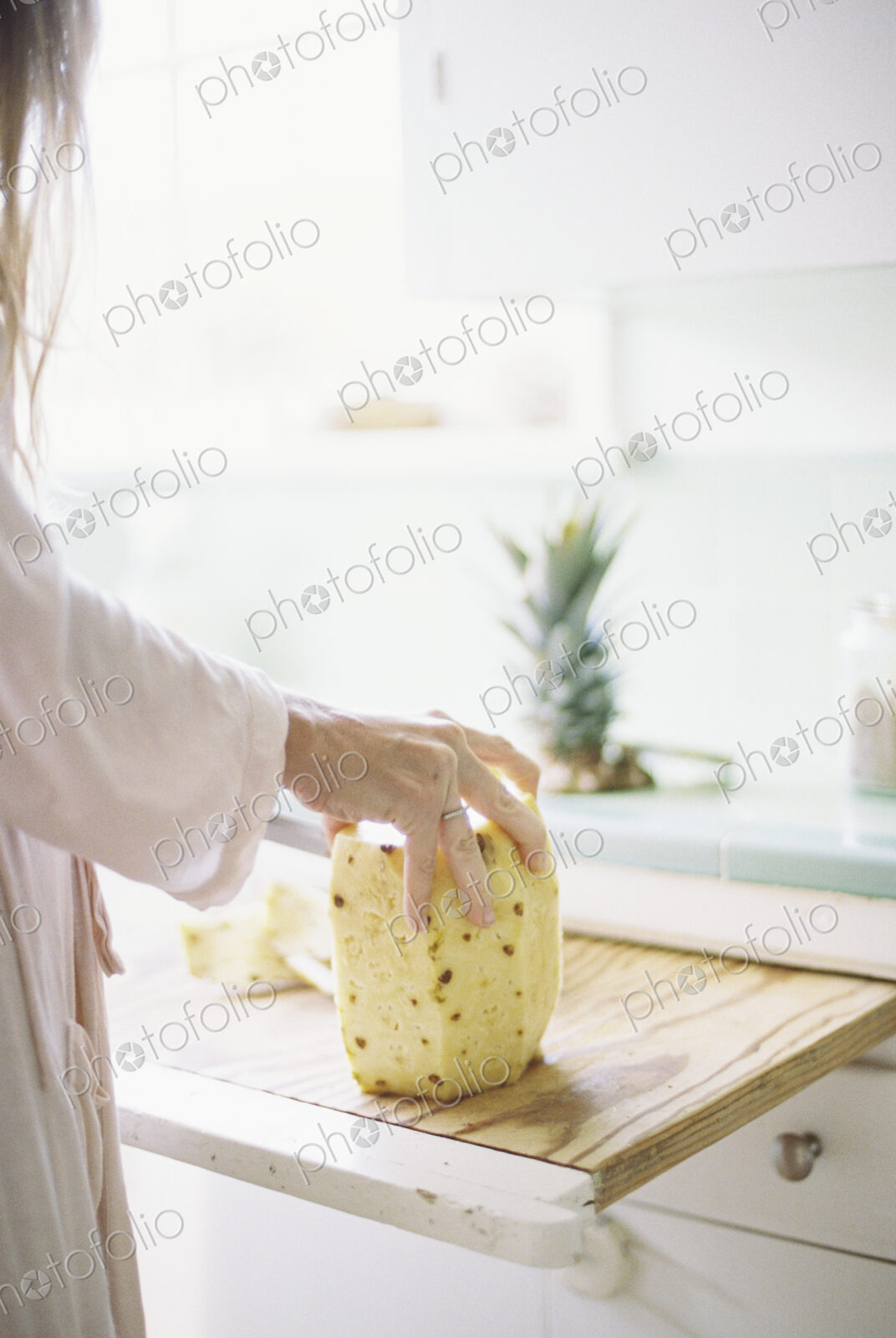 Woman standing in a kitchen, cutting a fresh pineapple.