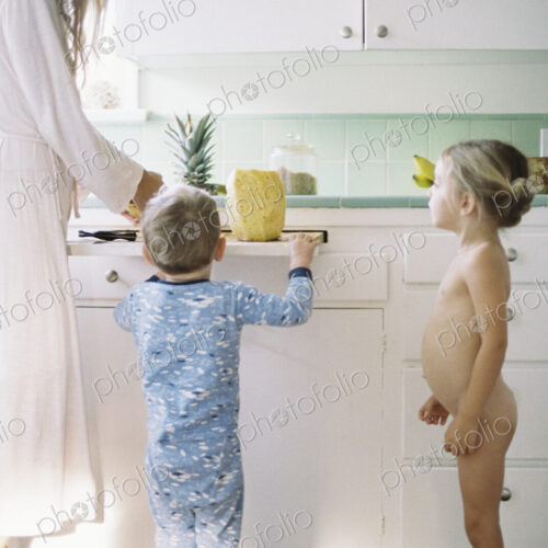 Woman standing in a kitchen, cutting a fresh pineapple for her children.