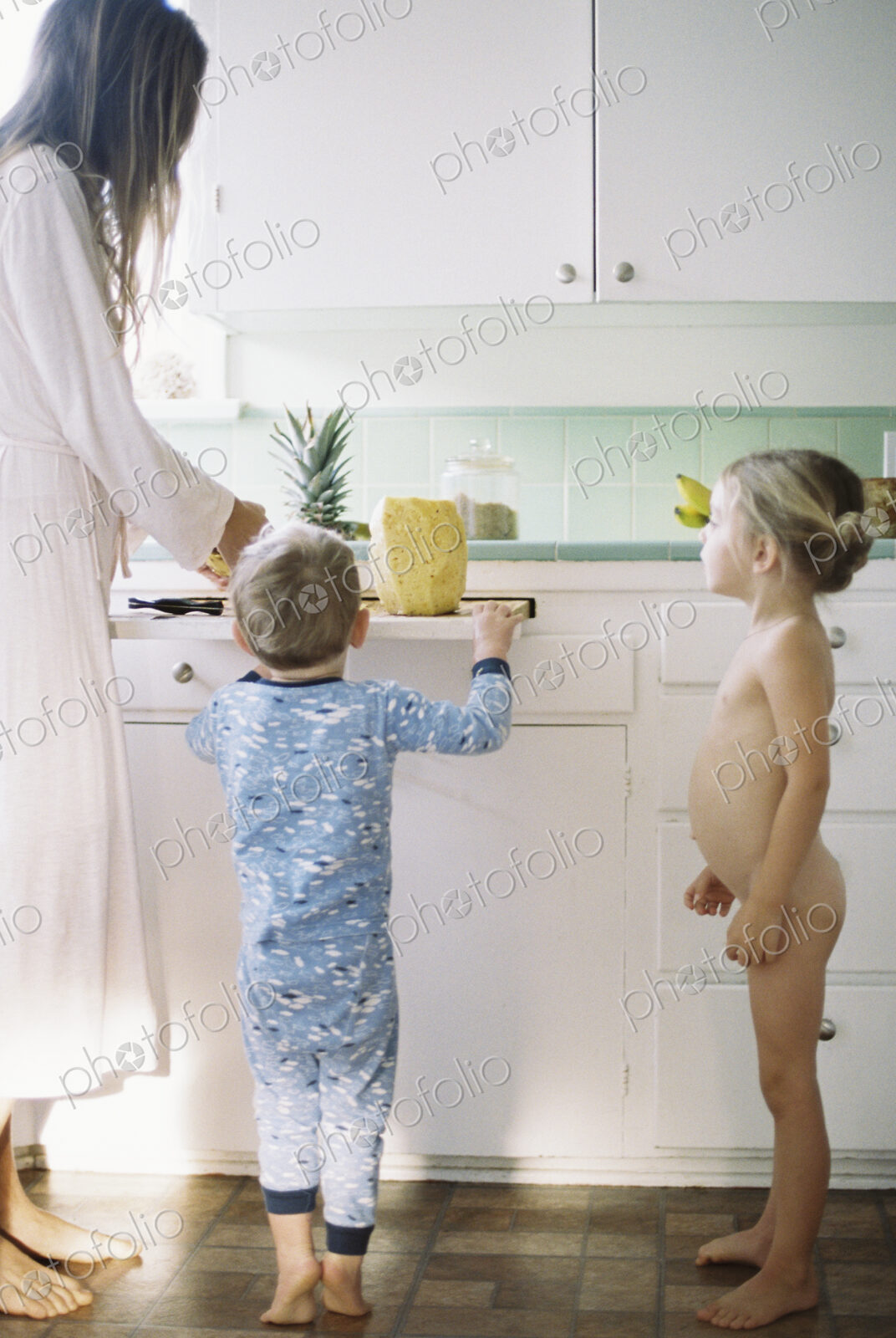 Woman standing in a kitchen, cutting a fresh pineapple for her children.