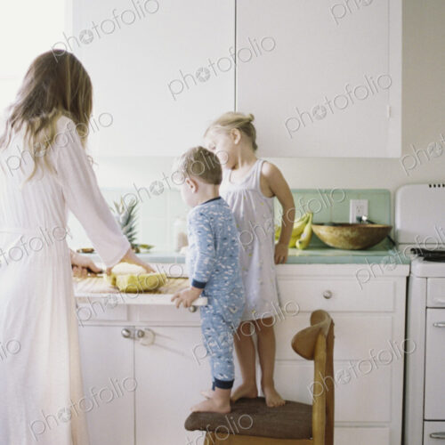 Woman standing in a kitchen, cutting a fresh pineapple for her children.