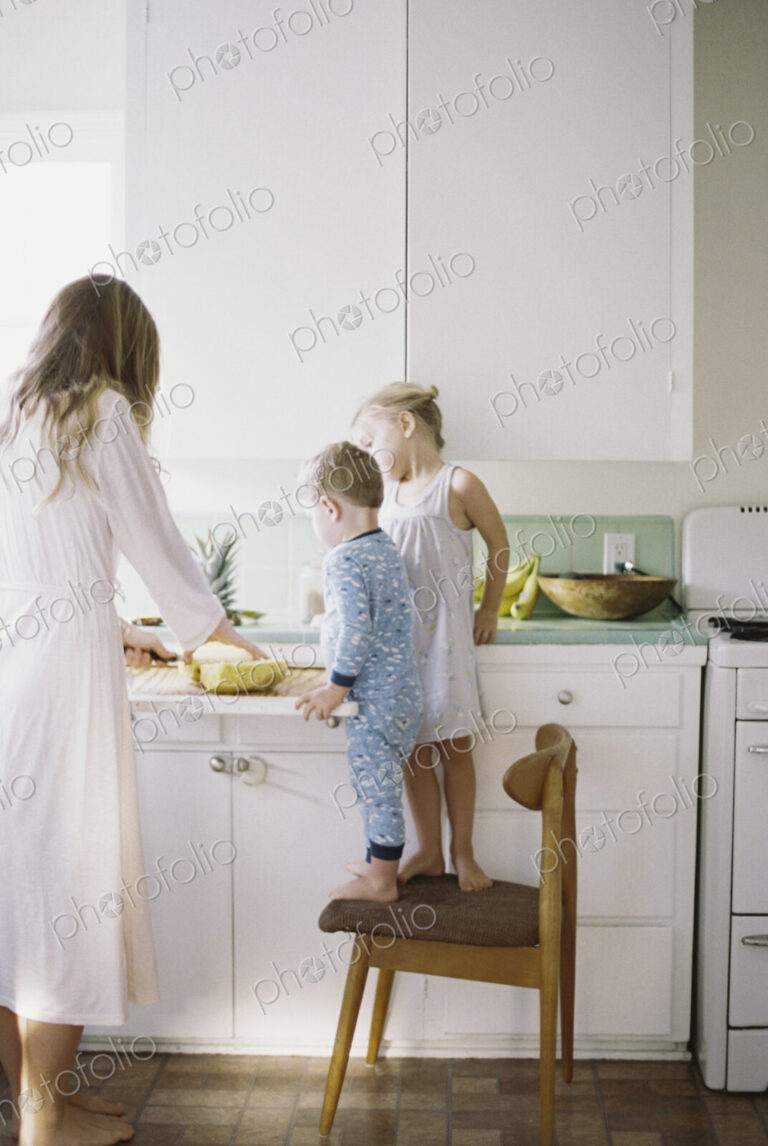 Woman standing in a kitchen, cutting a fresh pineapple for her children.