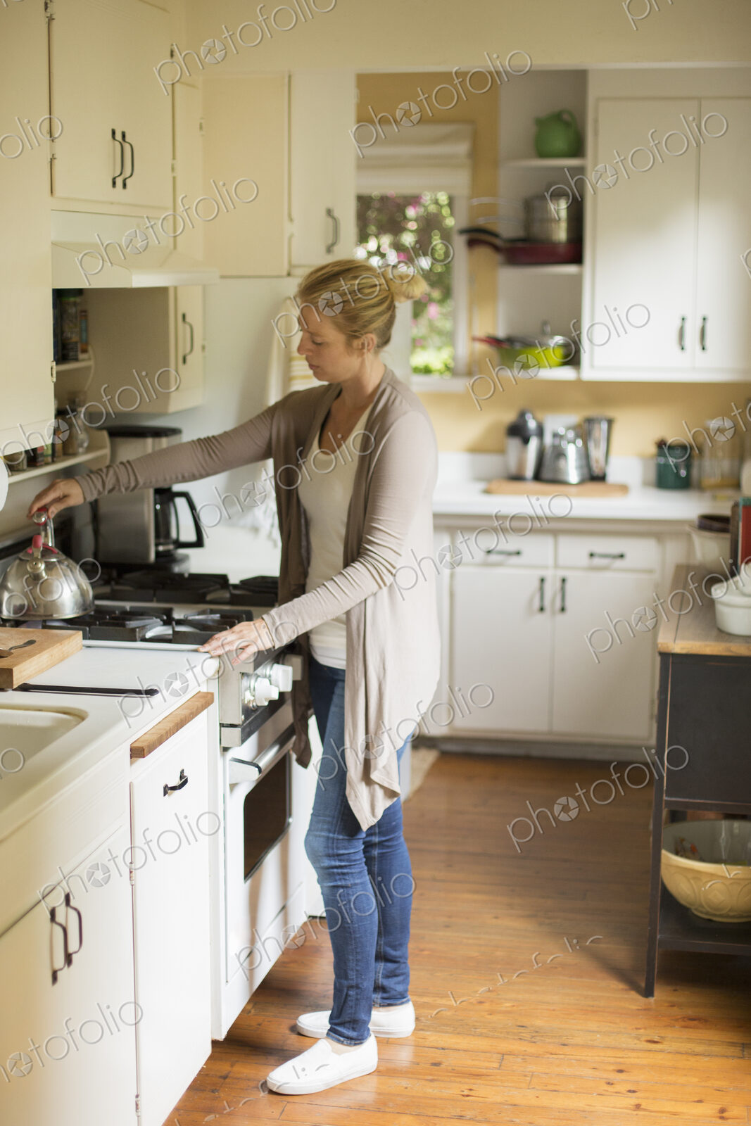 Woman standing in a kitchen, placing a kettle on a stove.