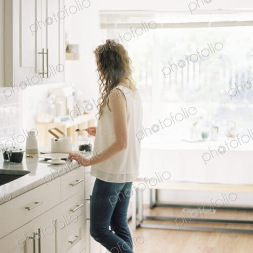Woman standing in a kitchen preparing a pot of tea.