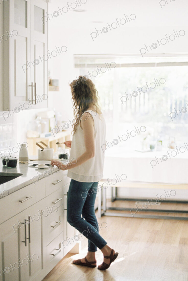 Woman standing in a kitchen preparing a pot of tea.