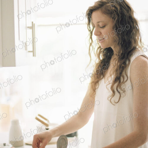Woman standing in a kitchen preparing a pot of tea.