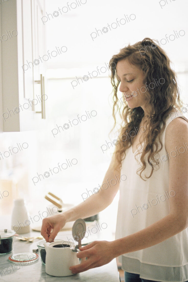 Woman standing in a kitchen preparing a pot of tea.