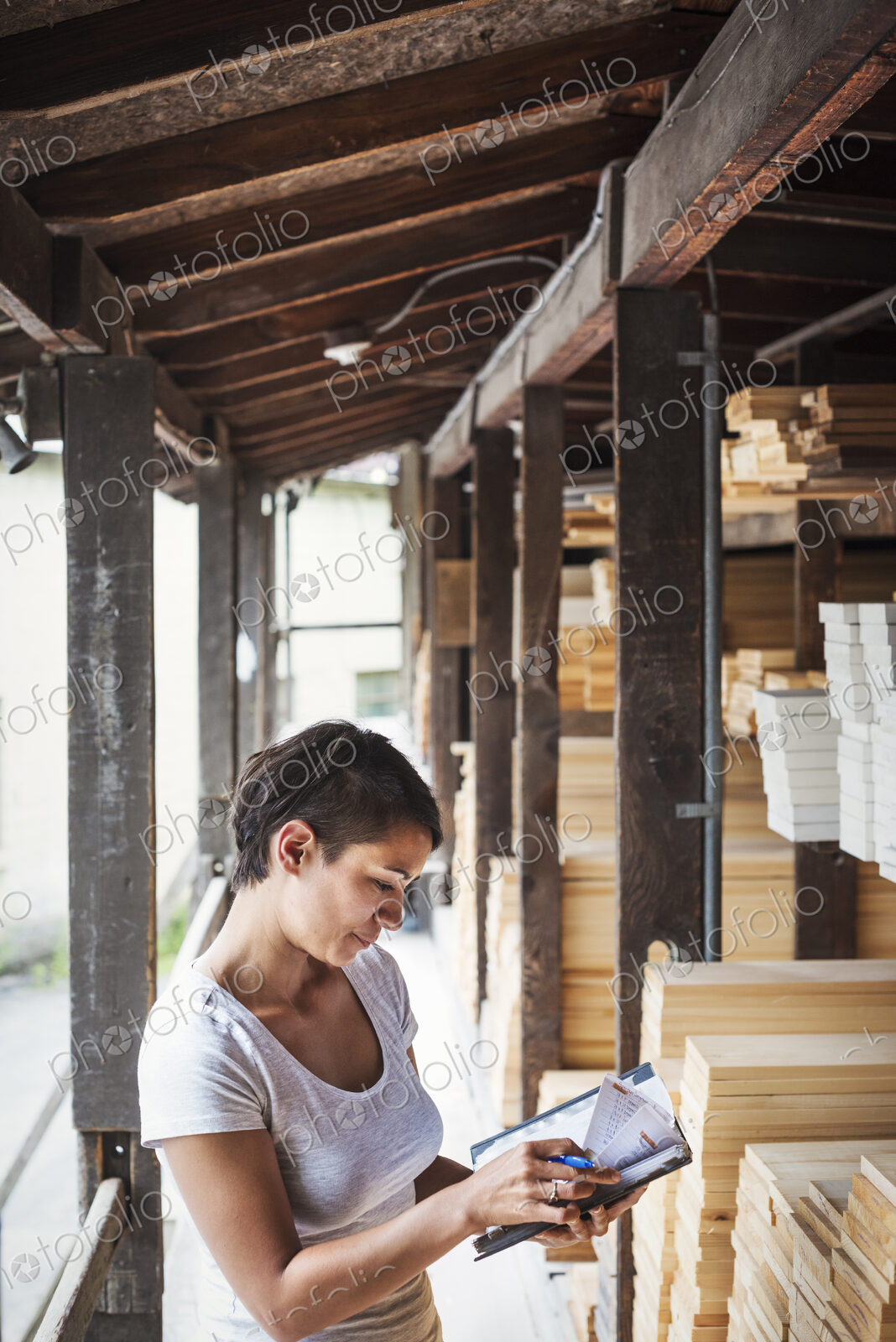 Woman standing in a lumber yard, holding a folder, checking notes.