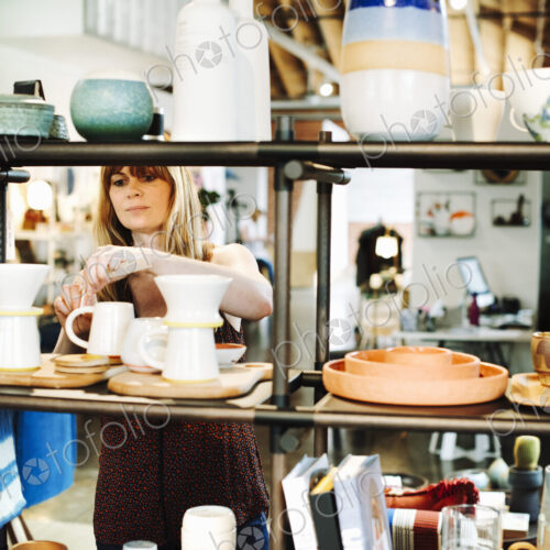 Woman standing in a shop, arranging ceramic objects on a shelf. Woman standing in a shop, arranging ceramic objects on a shelf.