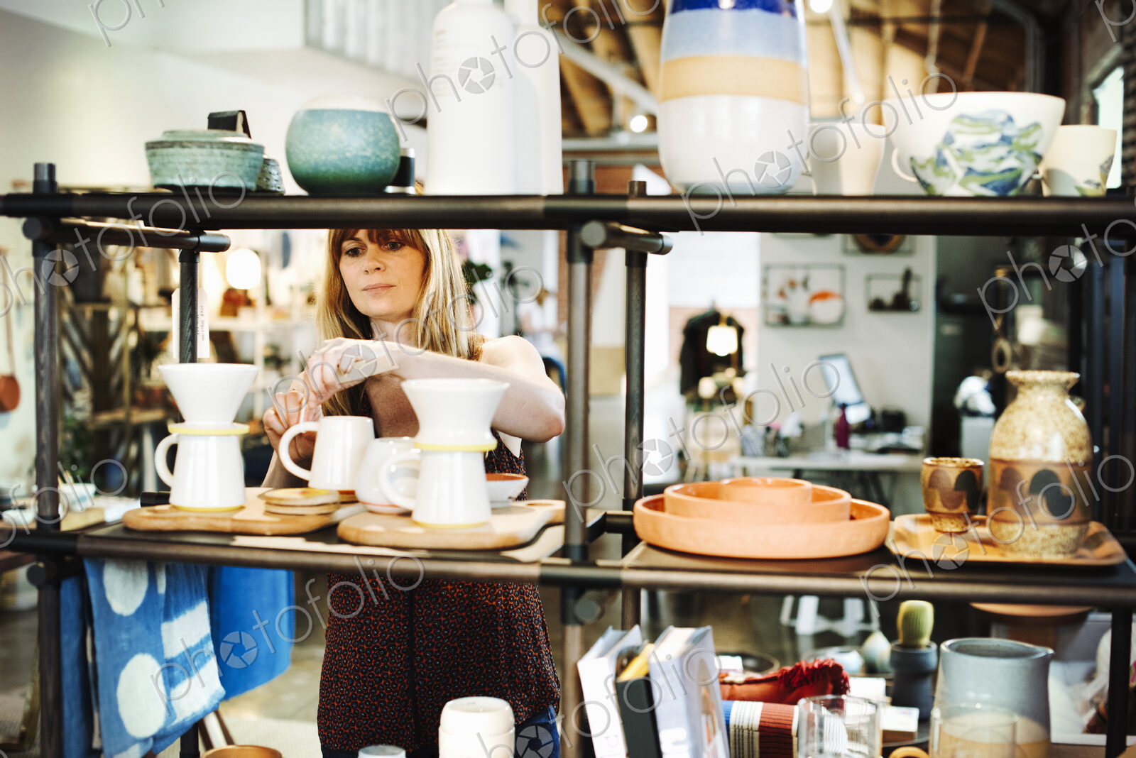 Woman standing in a shop, arranging ceramic objects on a shelf.