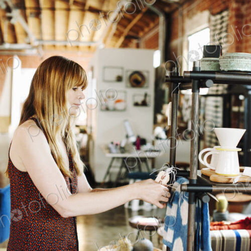 Woman standing in a shop, arranging merchandise on a shelf.