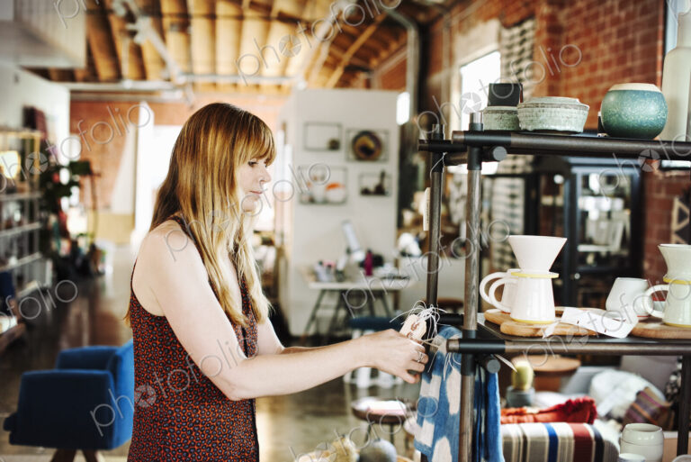 Woman standing in a shop, arranging merchandise on a shelf.