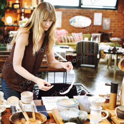 Woman standing in a shop, arranging merchandise on a table. Woman standing in a shop, arranging merchandise on a table.