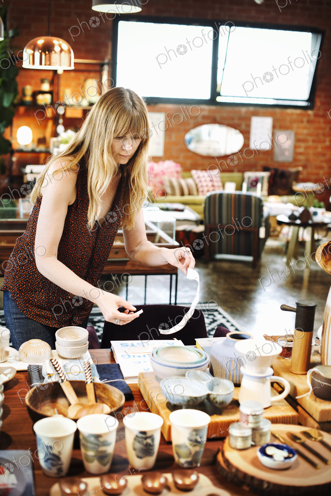 Woman standing in a shop, arranging merchandise on a table.