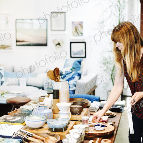 Woman standing in a shop, arranging merchandise on a table. Woman standing in a shop, arranging merchandise on a table.