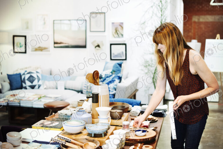 Woman standing in a shop, arranging merchandise on a table.