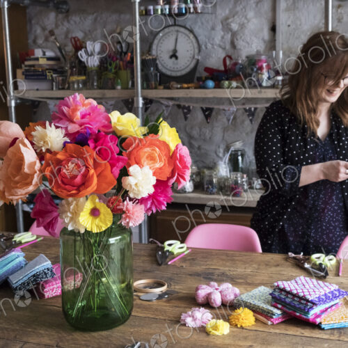 Woman standing in a workshop, bunch of colourful handcrafted fabric flowers in a vase…